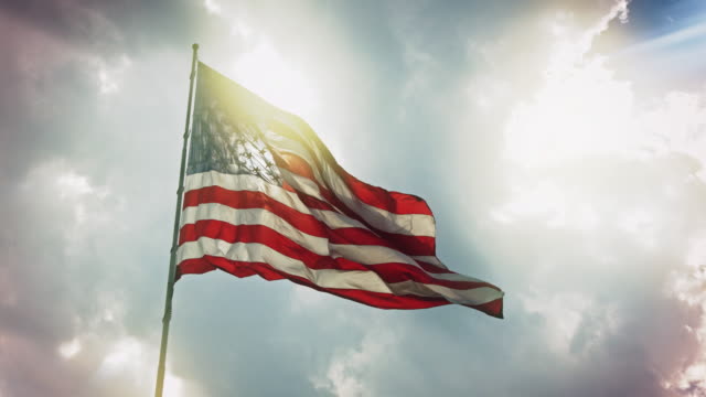 Slow motion clip of the Flag of the United States, also known as the Stars and Stripes, the Star Spangled Banner and Old Glory, flying in a breeze, with sunlight shining through its fabric.