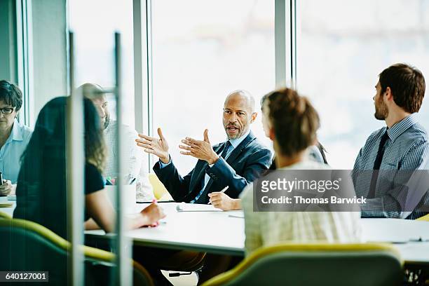 mature businessman leading meeting in office - konferenzraum stock-fotos und bilder