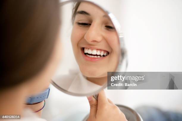 teenage girl looking at her teeth in the mirror - dental equipment stockfoto's en -beelden