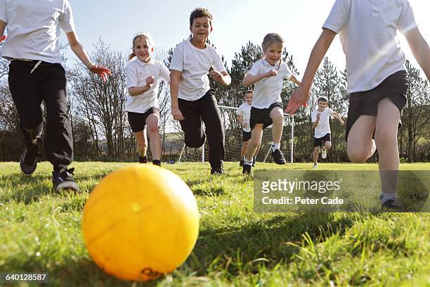 school children running for ball in field - boyshorts fotografías e imágenes de stock
