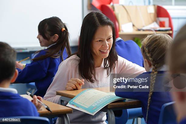 teacher helping pupil in classroom - elementary school supplies stock pictures, royalty-free photos & images