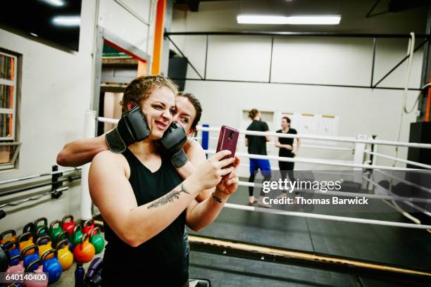 two female fighters taking self portrait with smartphone after training session in gym - funny boxing stock-fotos und bilder