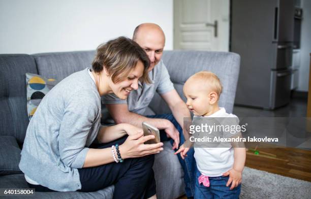 eltern zeigen ihrem kind bilder auf einem smartphone - alexandra iakovleva stock-fotos und bilder