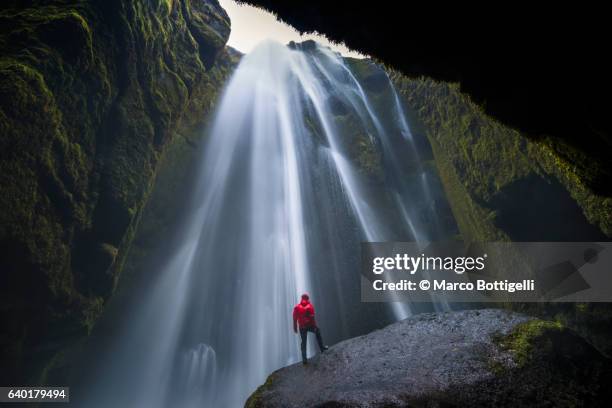 man with red coast standing on top of a rock under gljúfrafoss waterfall, southern iceland, iceland, northern europe. - cataract stock pictures, royalty-free photos & images