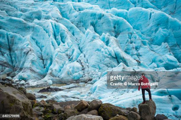 a man with red coat standing on top of a rock admiring the view of a glacier in skaftafell national park, eastern iceland, northern europe. - vatnajokull - fotografias e filmes do acervo