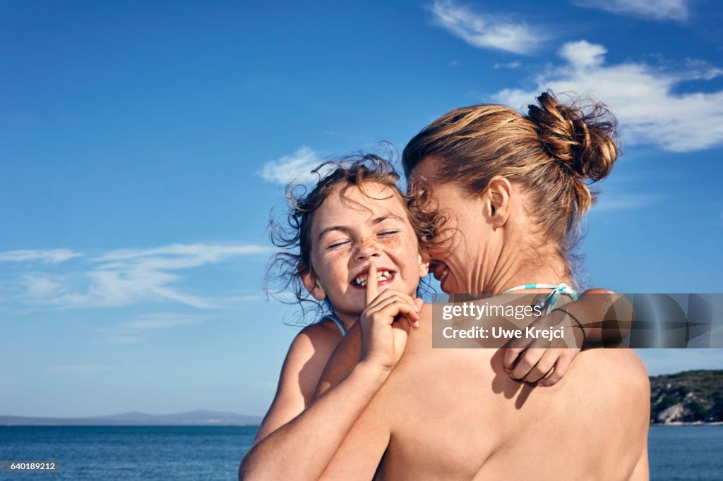 Girl hugging her mother on beach, smiling