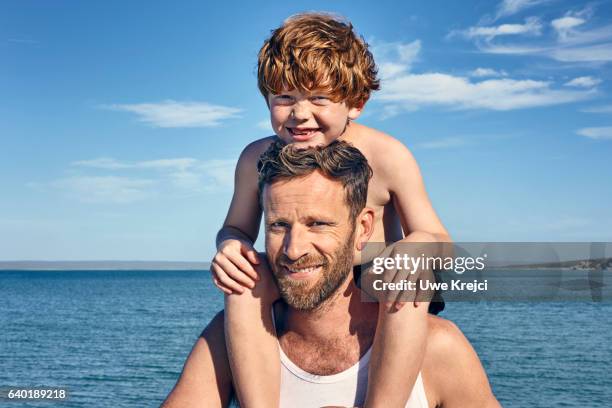 father carrying son on shoulders - mann mit kind auf den schultern stock-fotos und bilder