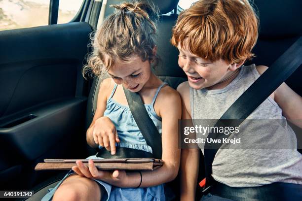 boy and girl on rear seat of car, playing on tablet - girl in car with ipad stock-fotos und bilder