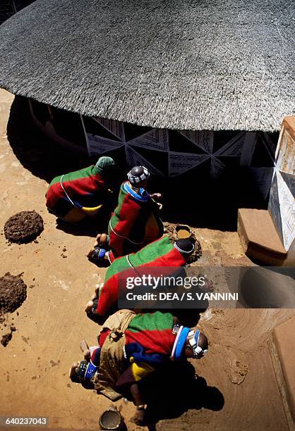 Men putting down flooring in front of a rondavel in a Ndebele village, South Africa.