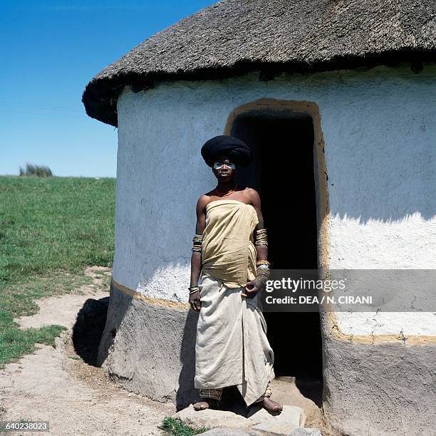 Xhosa girl with her face painted, wearing clothes and traditional jewellery, in front of a hut, Transkei, Eastern Cape, South Africa.