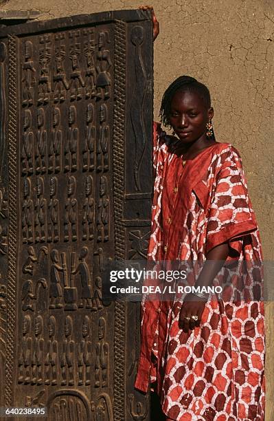 Young Dogon woman next to a carved door, Sangha village, Bandiagara Escarpment, Mali.