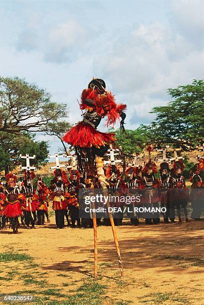 Dogon dancers, one of them on stilts, wearing Kanaga masks performing the Dama or masked funeral dance, Bandiagara Escarpment, Mali.