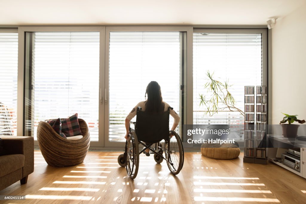 Young disabled woman in wheelchair at home, rear view.