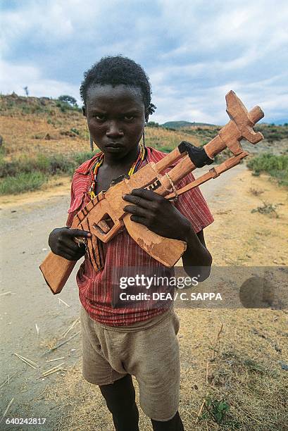 Child with wooden toy weapon, copied from a Kalashnikov rifle, near Konso, Ethiopia.