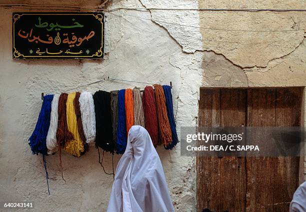 Woman wearing a burqa and skeins of wool hanging up, M'zab Valley, Ghardaia, Algeria.