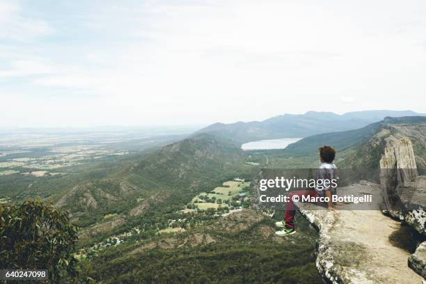 man sitting on a rock overhang at the boroka lookout, grampians national park, victoria, australia. - shoes top view stockfoto's en -beelden