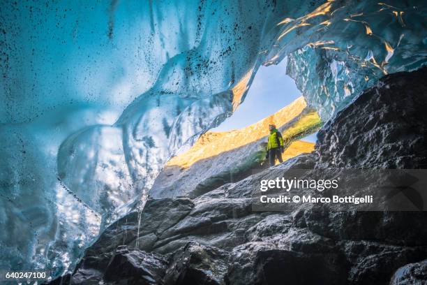 man standing at the entrance of a crystal ice cave in vatnajokull glacier, eastern iceland, iceland, northern europe. - crystal caves ストックフォトと画像