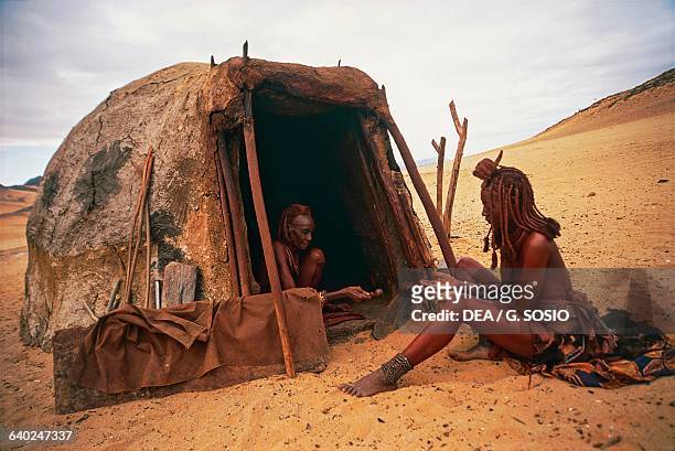 Himba women in front of a hut, Kunene region, Serra Cafema, Namibia.