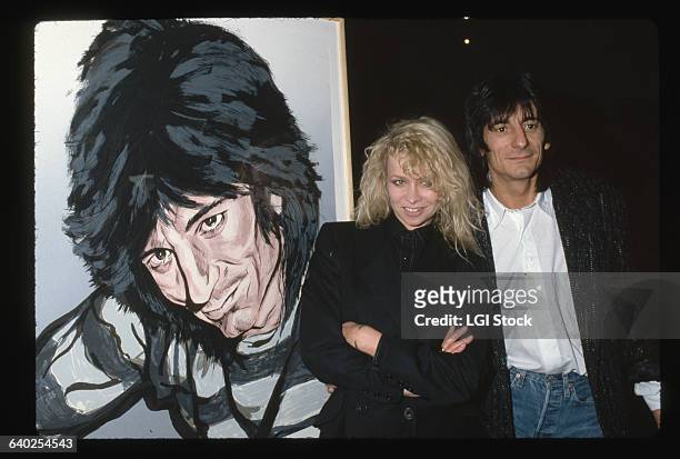 Rolling Stones guitarist Ron Wood stands with his girlfriend Jo Howard next to a painting of himself.