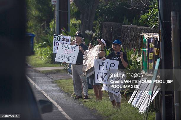 People are seen holding signs outside of Kailuana Place as US President Barack Obama's motorcade returns to his vacation compound from Marine Corps...
