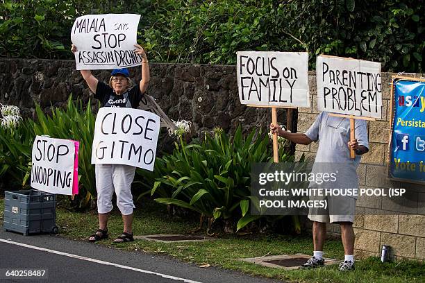 Protestors hold signs as U.S. President Barack Obama's motorcade returns to his vacation compound at Kailuana Place upon returning from a hiking the...