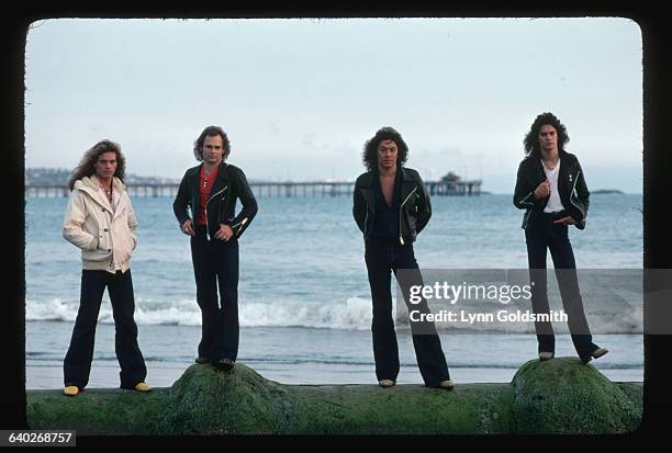 Photograph of the rock band, Van Halen. They are at the beach standing on algae covered seawall, Band members are left to right: David Lee Roth,...