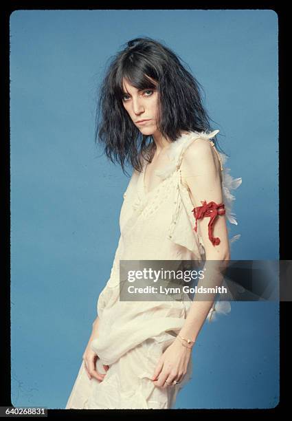 Punk rock singer and poet Patti Smith poses for a studio portrait. She wears feathers down her back, meant to suggest an angel's wings, and a red...