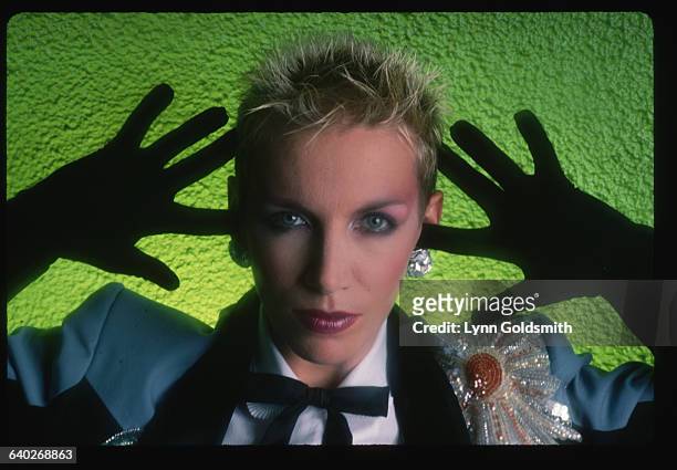 Annie Lennox of the Eurythmics is shown in a blue jacket with black gloves in front of a green background in this studio portrait.