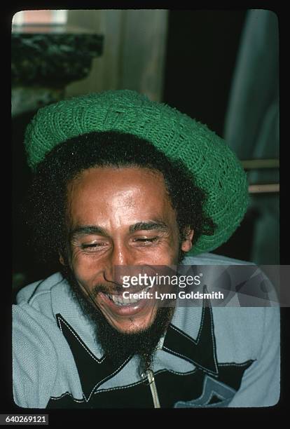 Close-up of Jamaican reggae musician Bob Marley laughing. He looks very relaxed and wears a green, crocheted cap over his dreadlocks.