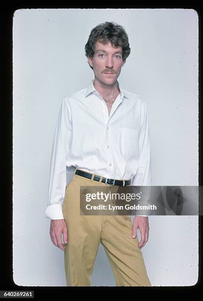 Posed full body shot of Fred Schneider of the B-52's. He is in a studio and he is wearing yellow pants, white shirt and he is shifted to the left.