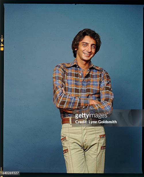 Singer/songwriter Barry Manilow is shown posed in a studio portrait. He wears a flannel shirt and tan pants with a brown woven belt. Undated.
