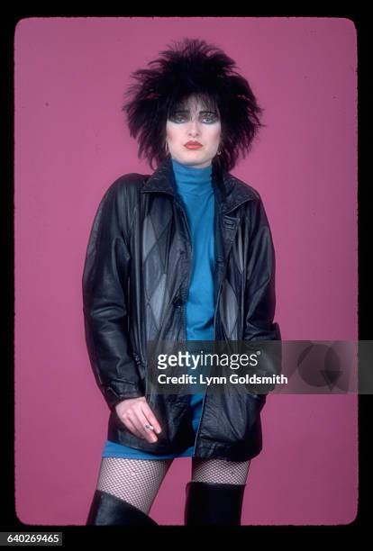 Picture shows a full length shot of Siouxsie Sioux, lead singer of Siouxsie & the Banshees. She is wearing a blue dress and a black leather jacket,...