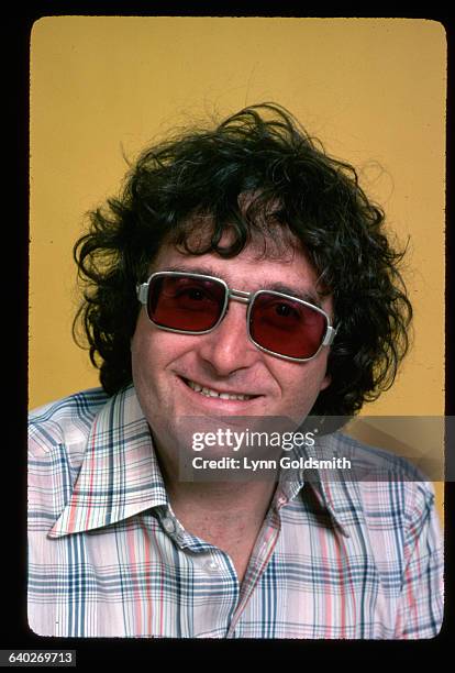 Singer/songwriter/composer Randy Newman is shown in a head and shoulders studio portrait, wearing a white, red and plaid shirt and sunglasses.