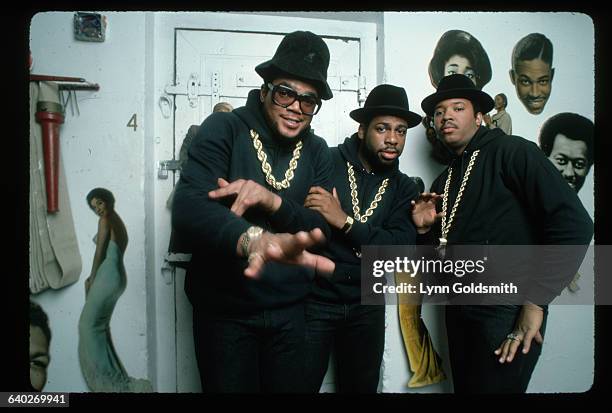 Rap group Run-DMC are shown posed in a white room, with what appears to be pictures of black entertainers on the wall. Left to right: DMC, Run and...