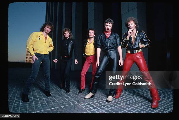 Outdoor portrait of Loverboy. Band members are shown full-length, posing outside a city building at dusk. Photograph, 1981.