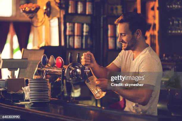 smiling bartender pouring beer from beer tap in a bar. - beer pump stock pictures, royalty-free photos & images