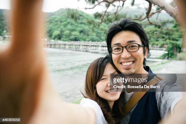 cheerful japanese couple taking selfie outdoors in a park - zelfportret stockfoto's en -beelden