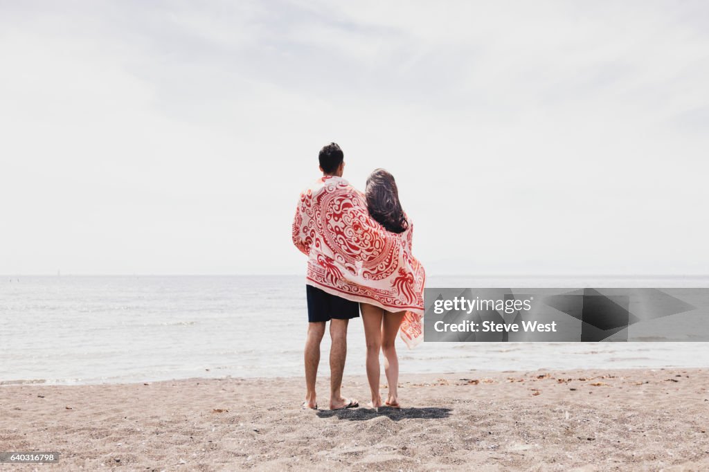 Couple Standing On The Beach Looking At The Ocean
