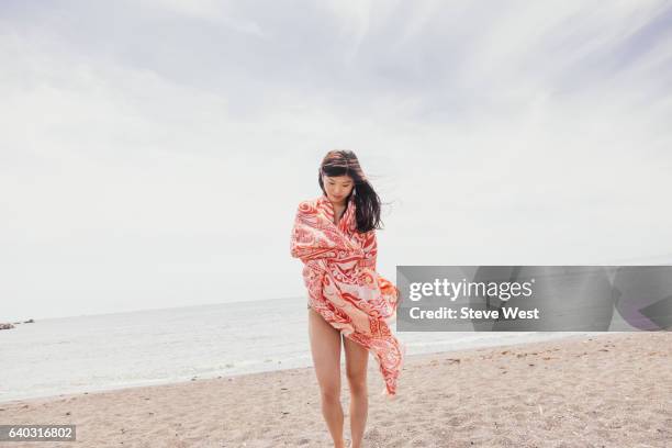 young woman walking on the beach wrapped in a sarong - sarong stock pictures, royalty-free photos & images