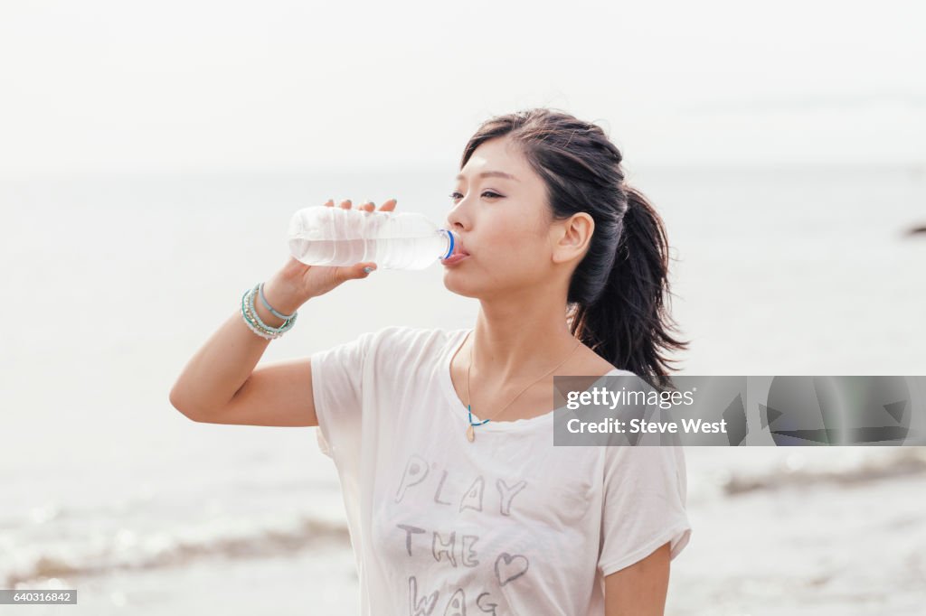 Young Athletic Asian Woman Drinking Water On The Beach