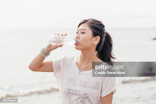 young athletic asian woman drinking water on the beach - west asia stock-fotos und bilder