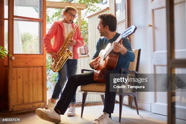 father and daugther playing the guitar at home. - saxophone stock pictures, royalty-free photos & images