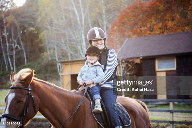 mother and son enjoying horse-riding together in pasture - zügel stock-fotos und bilder