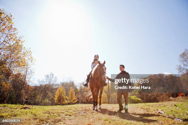 man leading mother and son who are riding on horse in pasture - enable horse stock-fotos und bilder