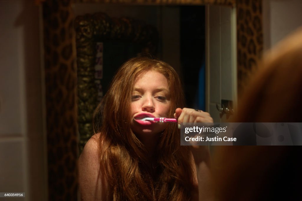 Woman brushing her teeth while looking in the mirror