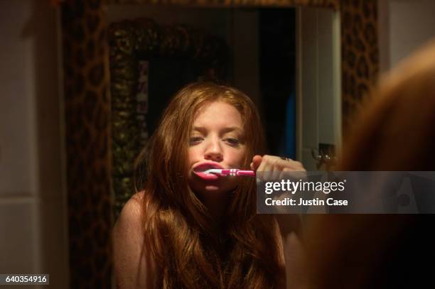 woman brushing her teeth while looking in the mirror - spazzolino da denti foto e immagini stock