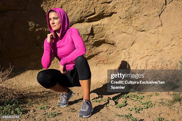 female runner wearing pink hoody crouching in front of rock - thousand oaks stock pictures, royalty-free photos & images
