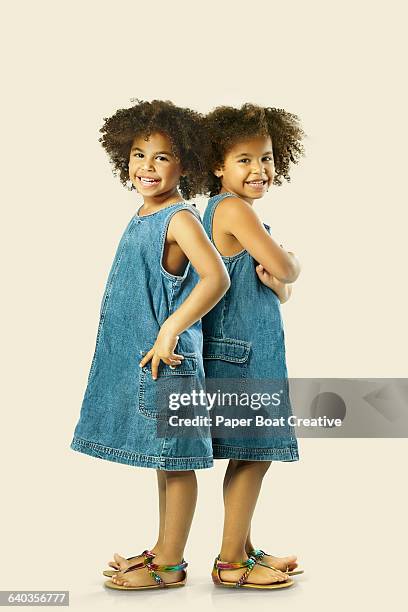 two identical twin sisters holding hands together - double denim stock-fotos und bilder