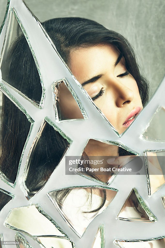 Lady with eyes closed looking sad; broken mirror