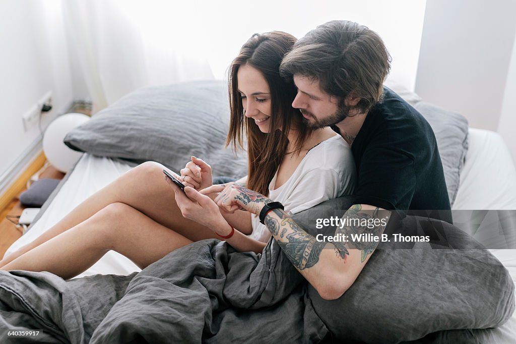 Young couple sitting in Bed using smart phone